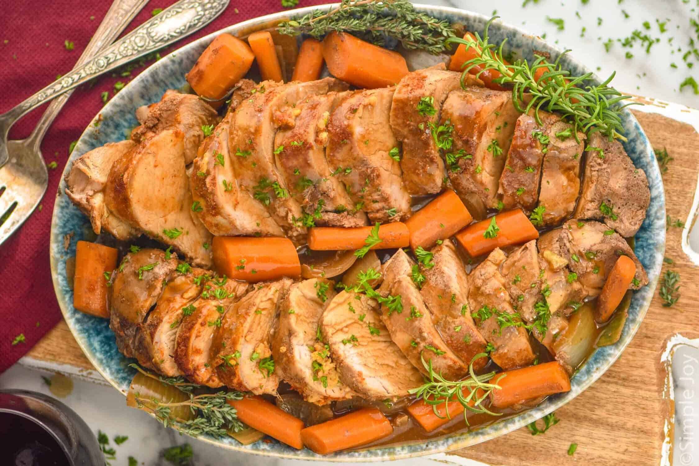 overhead of slow cooker pork tenderloin sliced an on a platter with cooked carrots