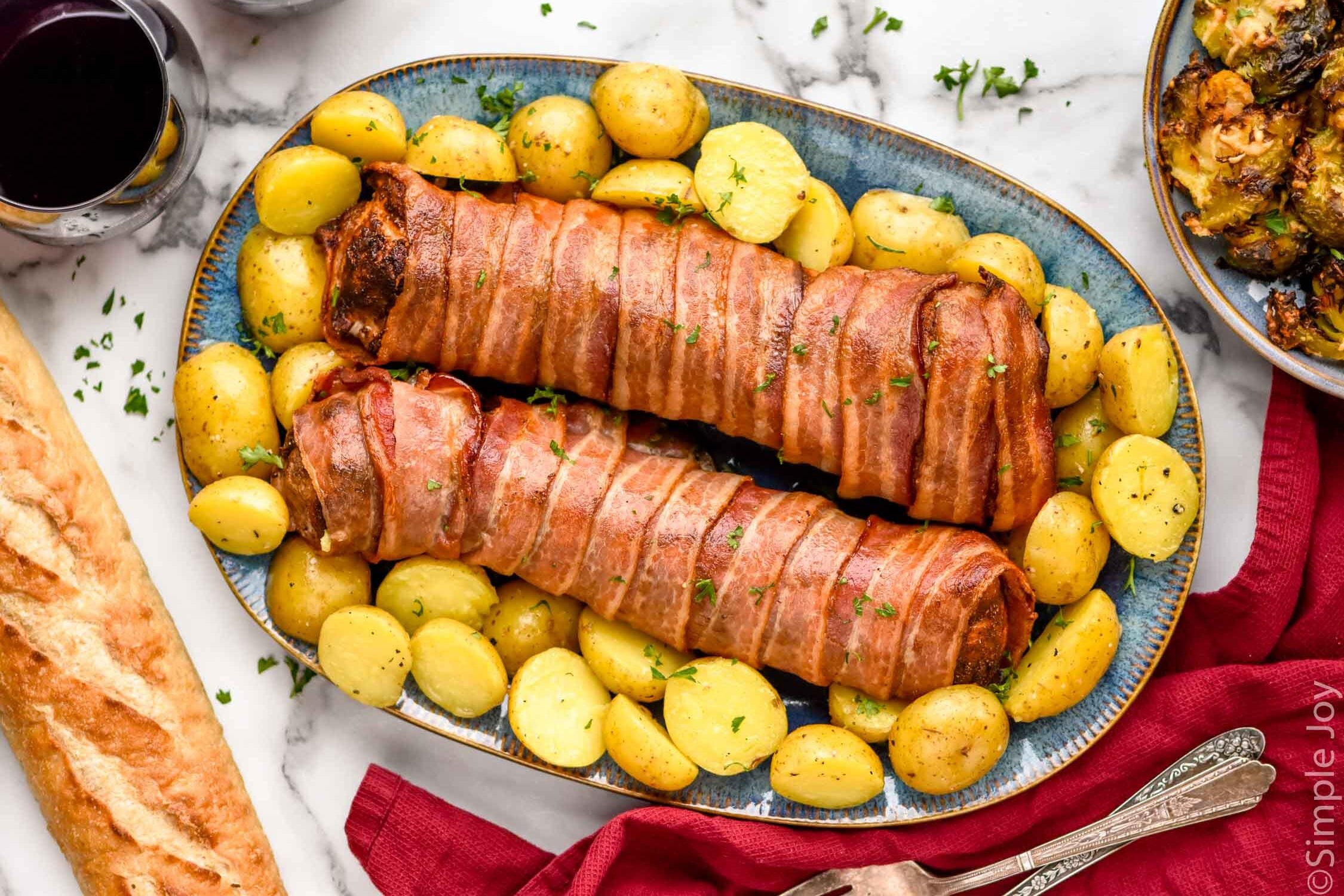 Overhead view of Bacon Wrapped Pork Tenderloin sliced and served on a platter with potatoes