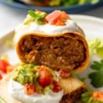 Inside of Baked Beef and Cheese Chimichangas topped with sour cream, diced tomatoes, guacamole, cilantro, and shredded lettuce