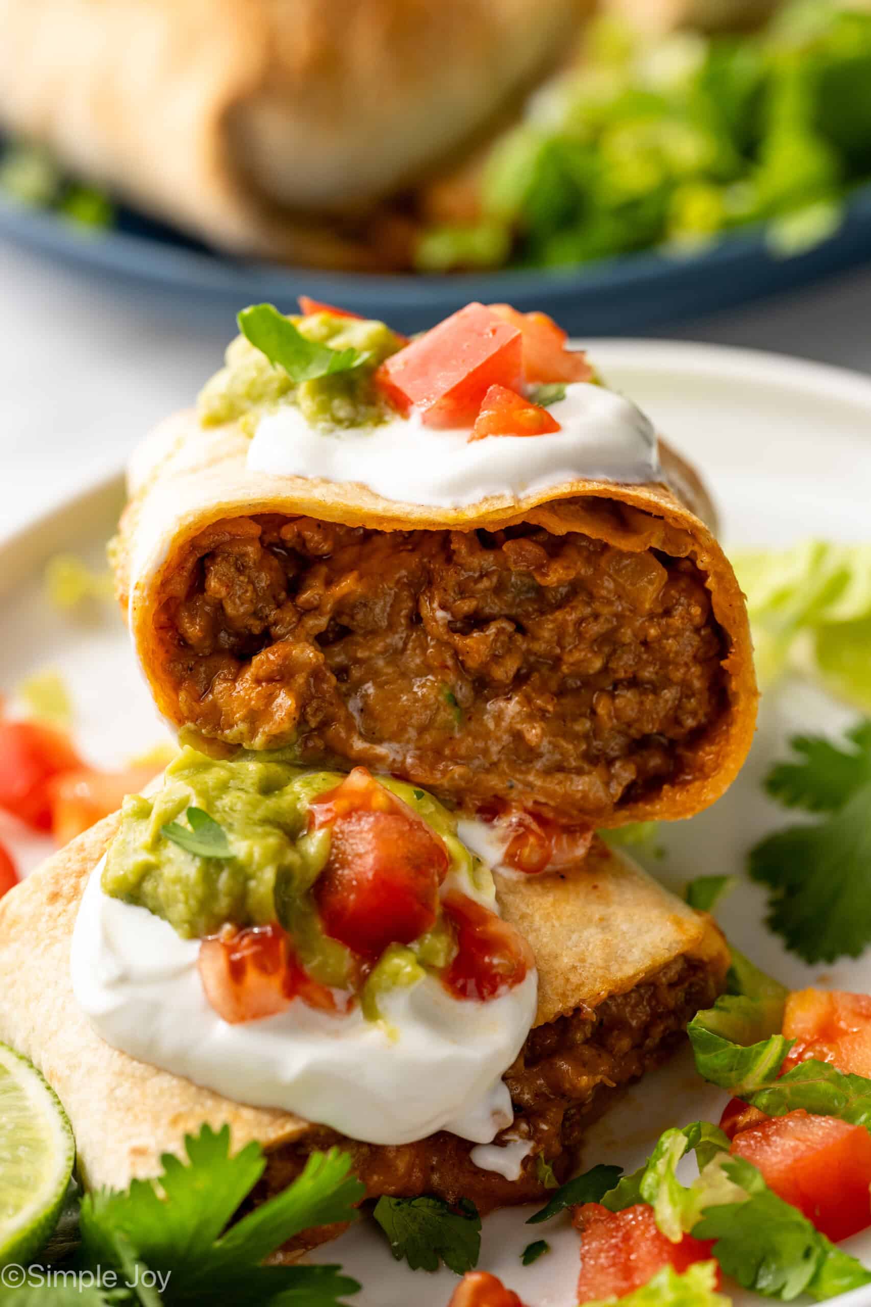Inside of Baked Beef and Cheese Chimichangas topped with sour cream, diced tomatoes, guacamole, cilantro, and shredded lettuce