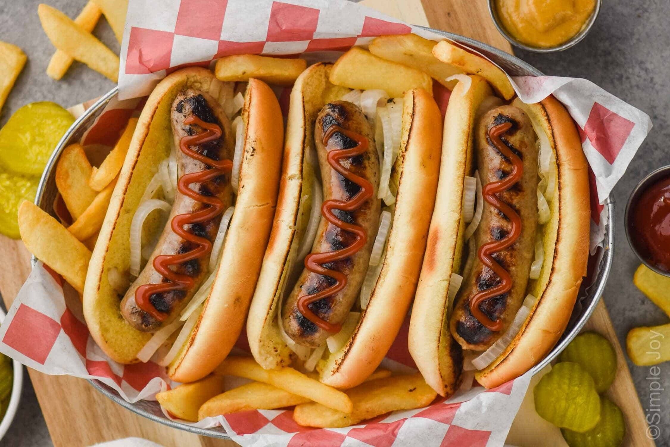 overhead of three beer brats in buns in a tray topped with ketchup