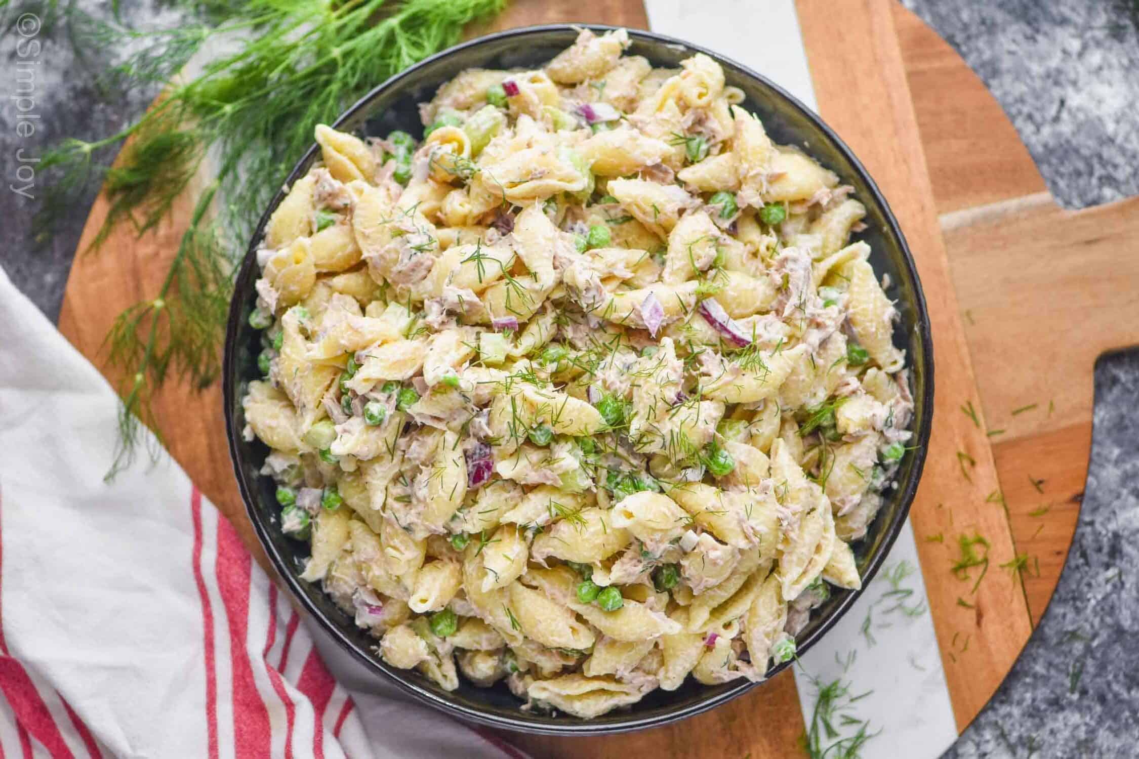 overhead photo of a serving bowl full of tuna pasta salad garnished with fresh dill with more fresh dill on the side