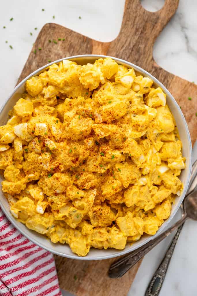 Overhead of bowl of Deviled Egg Potato Salad on wooden cutting board, two forks sitting beside.