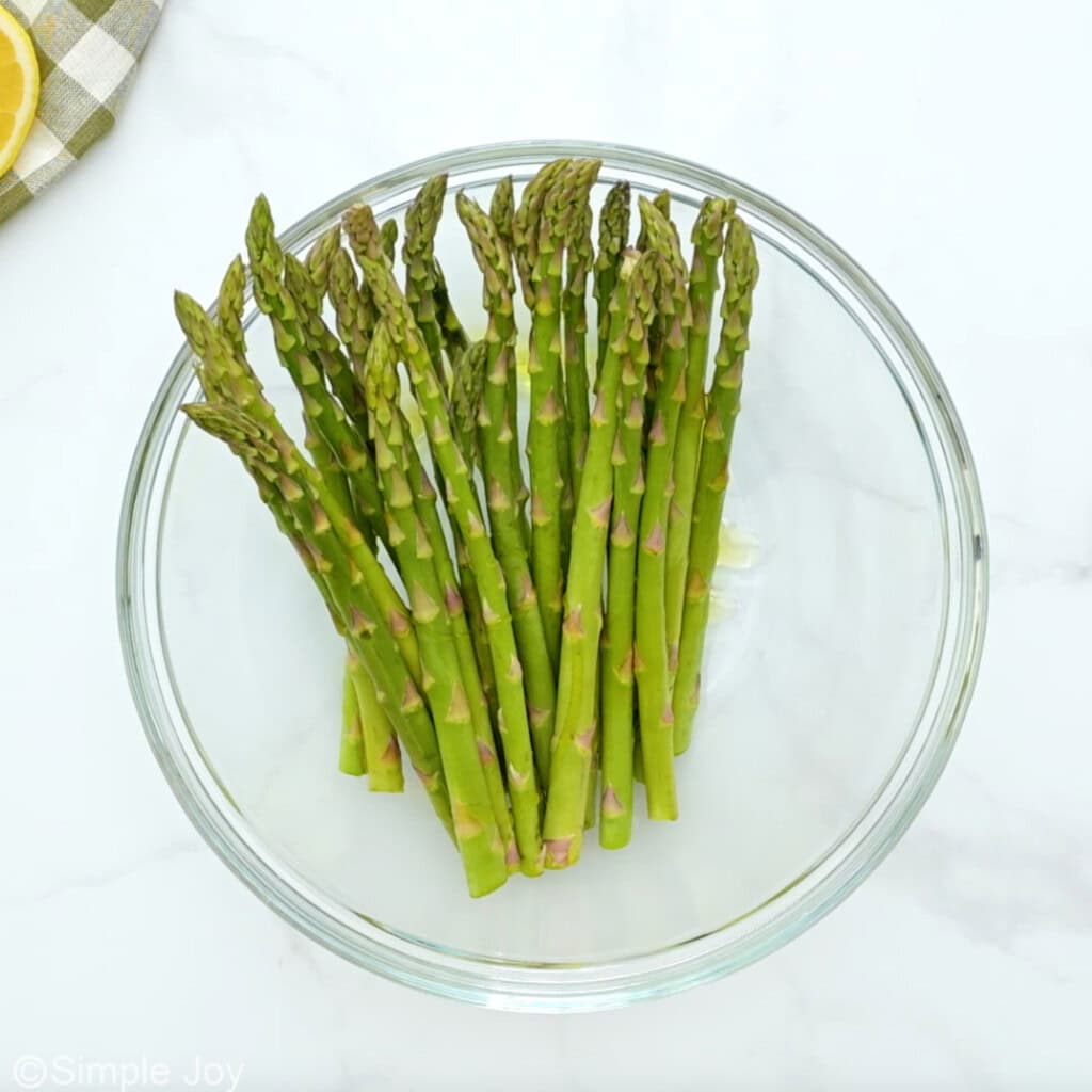 Overhead of glass bowl of asparagus and olive oil to make Air Fryer Cod recipe