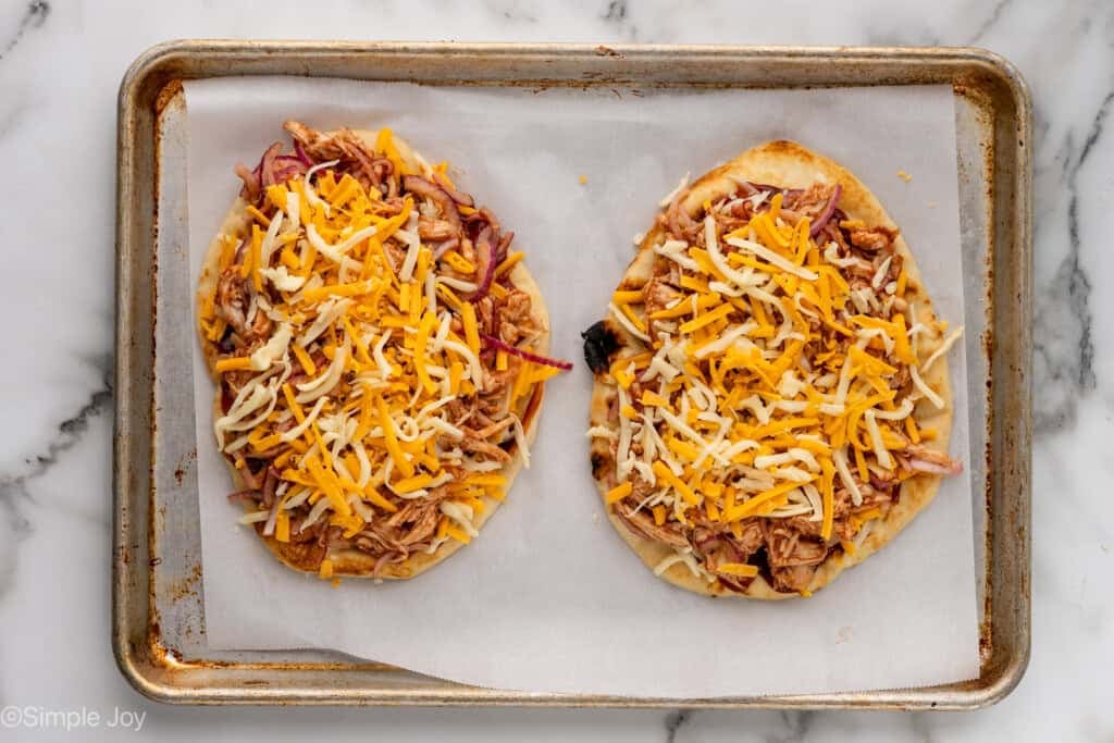Overhead of baking sheet with BBQ Chicken Flatbread Pizzas topped with shredded cheese