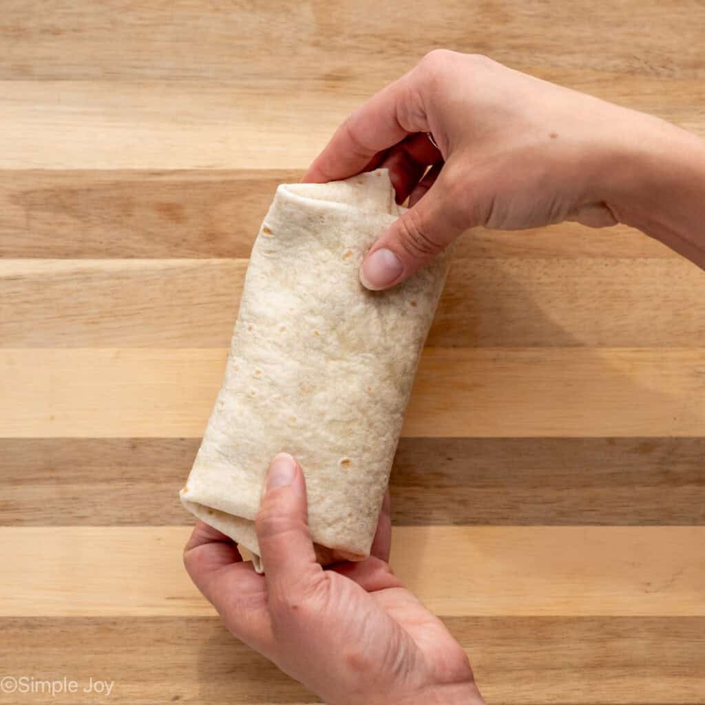 overhead of woman's hands rolling up tortilla of Baked Beef and Cheese Chimichangas ingredients