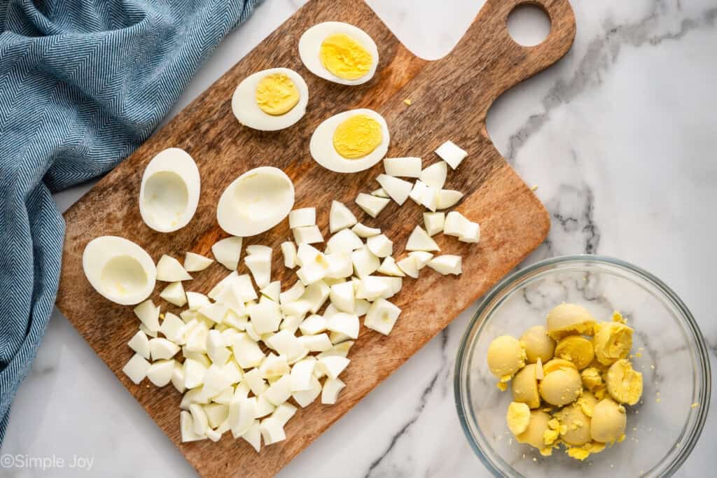 Overhead of hard boiled eggs on a wooden cutting board with bowl of egg yolks sitting beside to make Cottage Cheese Egg Salad recipe