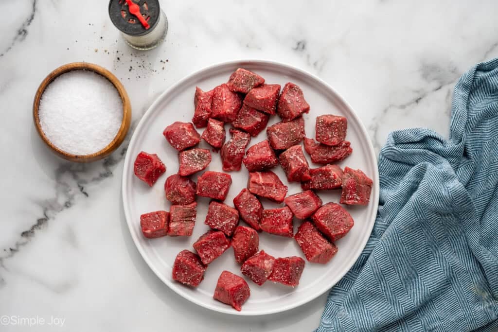 overhead of pieces of steak on a plate to make Garlic Butter Steak Bites with salt and pepper sitting beside