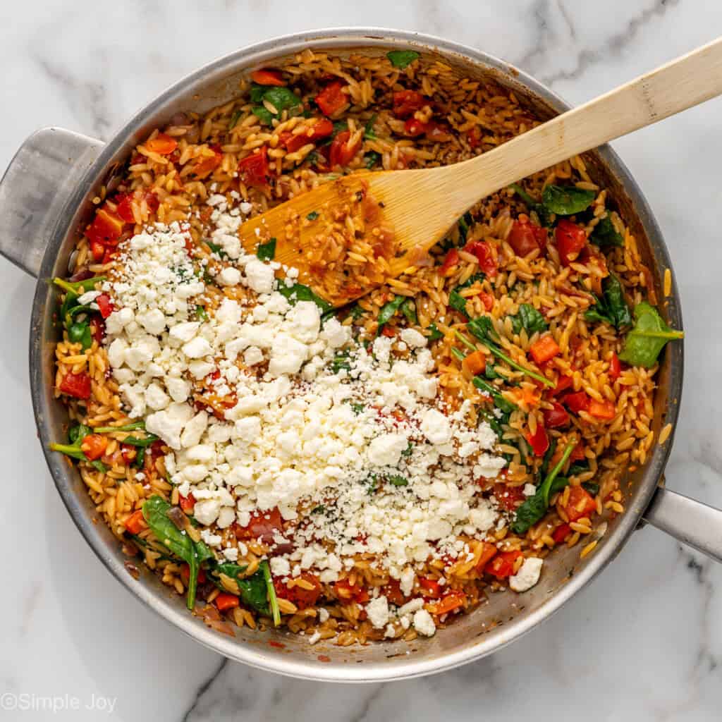 Overhead of skillet of Mediterranean Chicken and Orzo topped with feta cheese and a wooden spoon