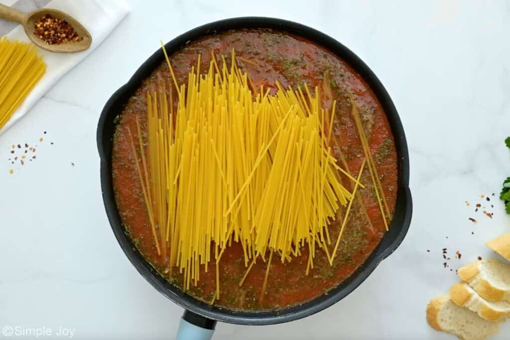 Overhead of skillet of one pot spaghetti ingredients topped with spaghetti noodles