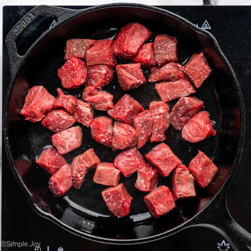 Overhead of pieces of seasoned steak in a skillet to make Garlic Butter Steak Bites recipe