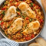 Overhead of skillet of Mediterranean Chicken and Orzo with sliced baguette sitting beside.