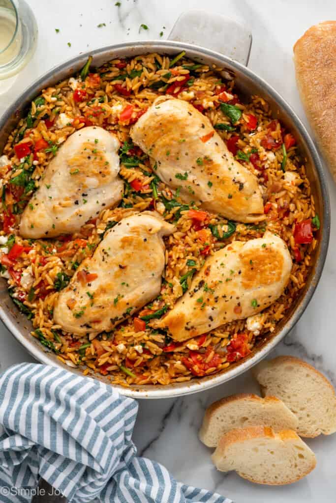 Overhead of skillet of Mediterranean Chicken and Orzo with sliced baguette sitting beside.