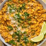 Overhead of bowl of Mexican Street Corn Dip garnished with chopped cilantro and lime wedges, tortilla chips sitting beside