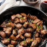 Skillet of Garlic Butter Steak Bites with two glasses of red wine in background