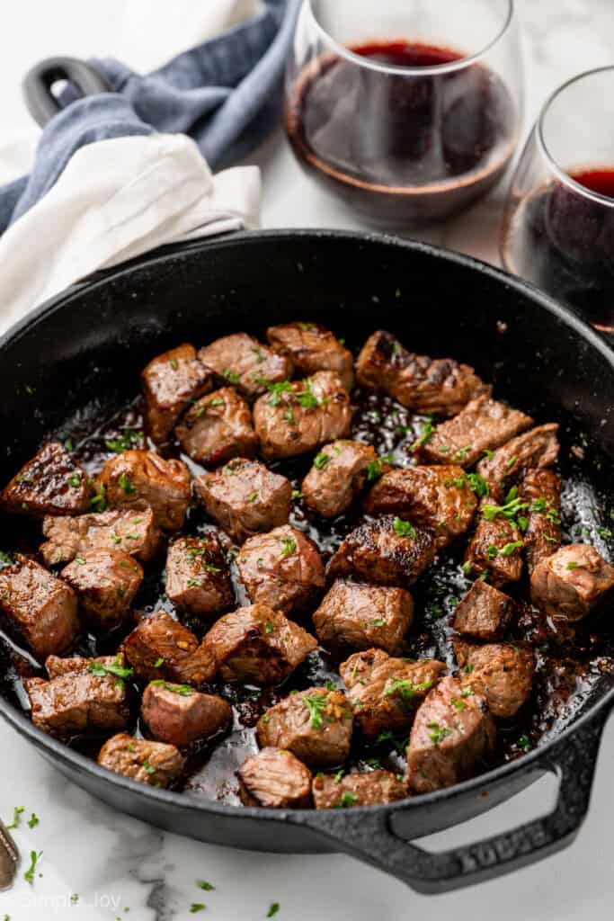Skillet of Garlic Butter Steak Bites with two glasses of red wine in background