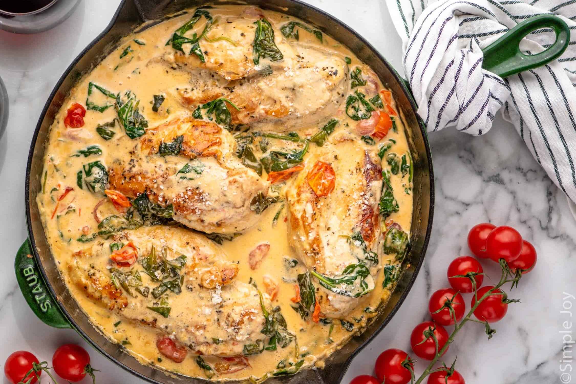 Overhead view of a skillet of Tuscan Chicken with cherry tomatoes beside.
