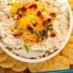 Pinterest graphic for crack dip. Image shows overhead of bowl of crack dip garnished with shredded cheese, bacon, and chives surrounded by crackers. Says "crazy good crack dip recipe simplejoy.com"