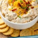 Pinterest graphic for Crack Dip. Image shows a bowl of crack dip garnished with shredded cheese, diced bacon, and chives, surrounded by crackers. Says "crack dip recipe simplejoy.com"