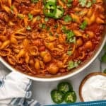 Pinterest graphic for One Pan Cheesy Taco Pasta. Image shows overhead of skillet of One Pan Cheesy Taco Pasta with cilantro and diced jalapeƱo. Says "One Pan 30 minute Taco Pasta Recipe simplejoy.com"