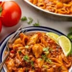 Pinterest graphic for One Pan Cheesy Taco Pasta. Says "30 minute taco pasta recipe simplejoy.com" Image shows a bowl of One Pan Cheesy Taco Pasta garnished with fresh cilantro and lime wedges