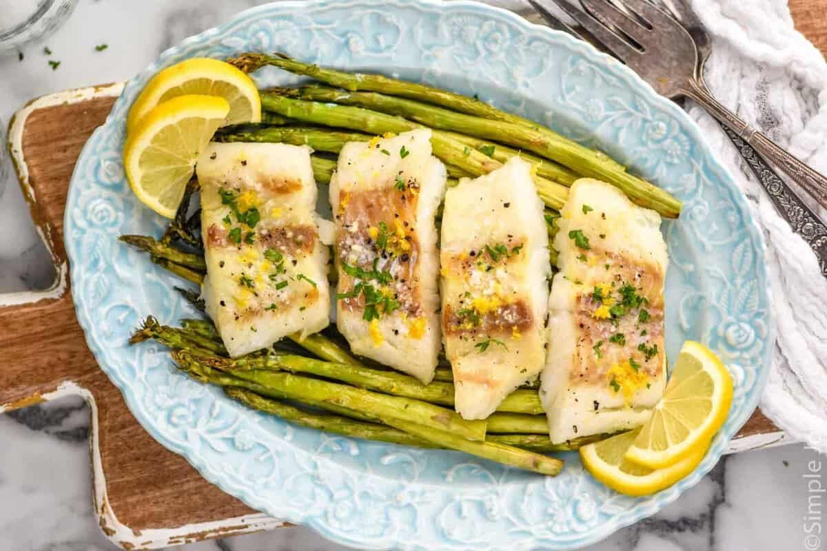 Overhead photo of a platter of Air Fryer Cod, asparagus, and lemon slices.