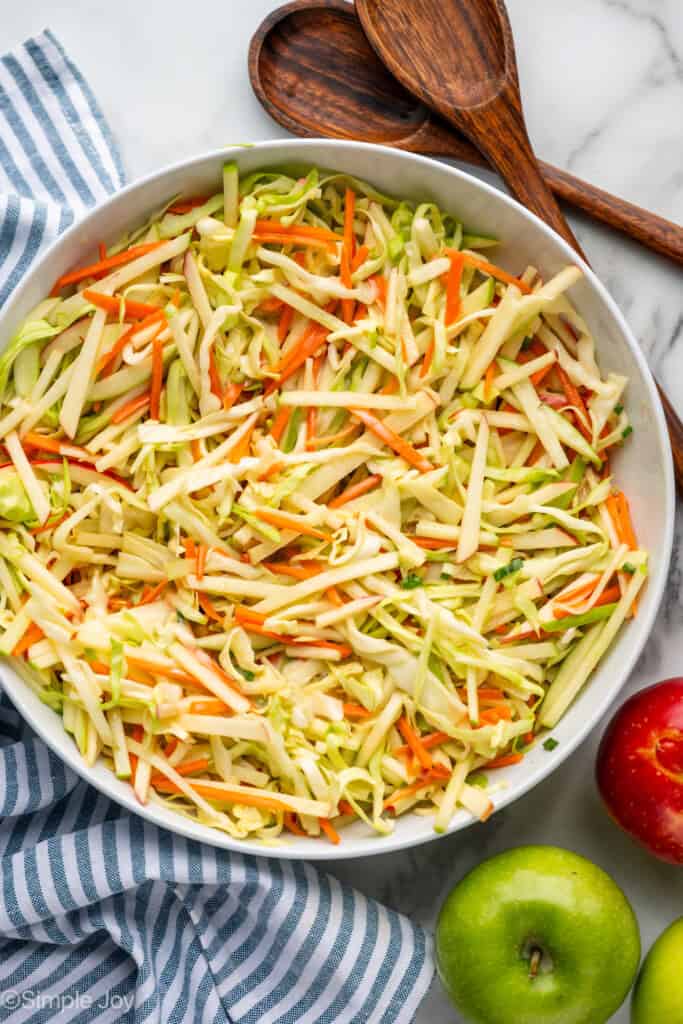 Overhead of bowl of apple slaw with red and green apples and wooden spoons sitting beside