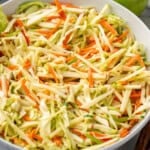 Bowl of apple slaw with red and green apples sitting in background
