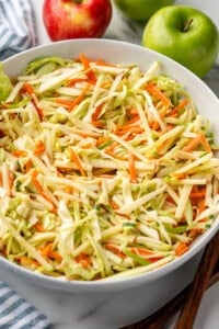 Bowl of apple slaw with red and green apples sitting in background