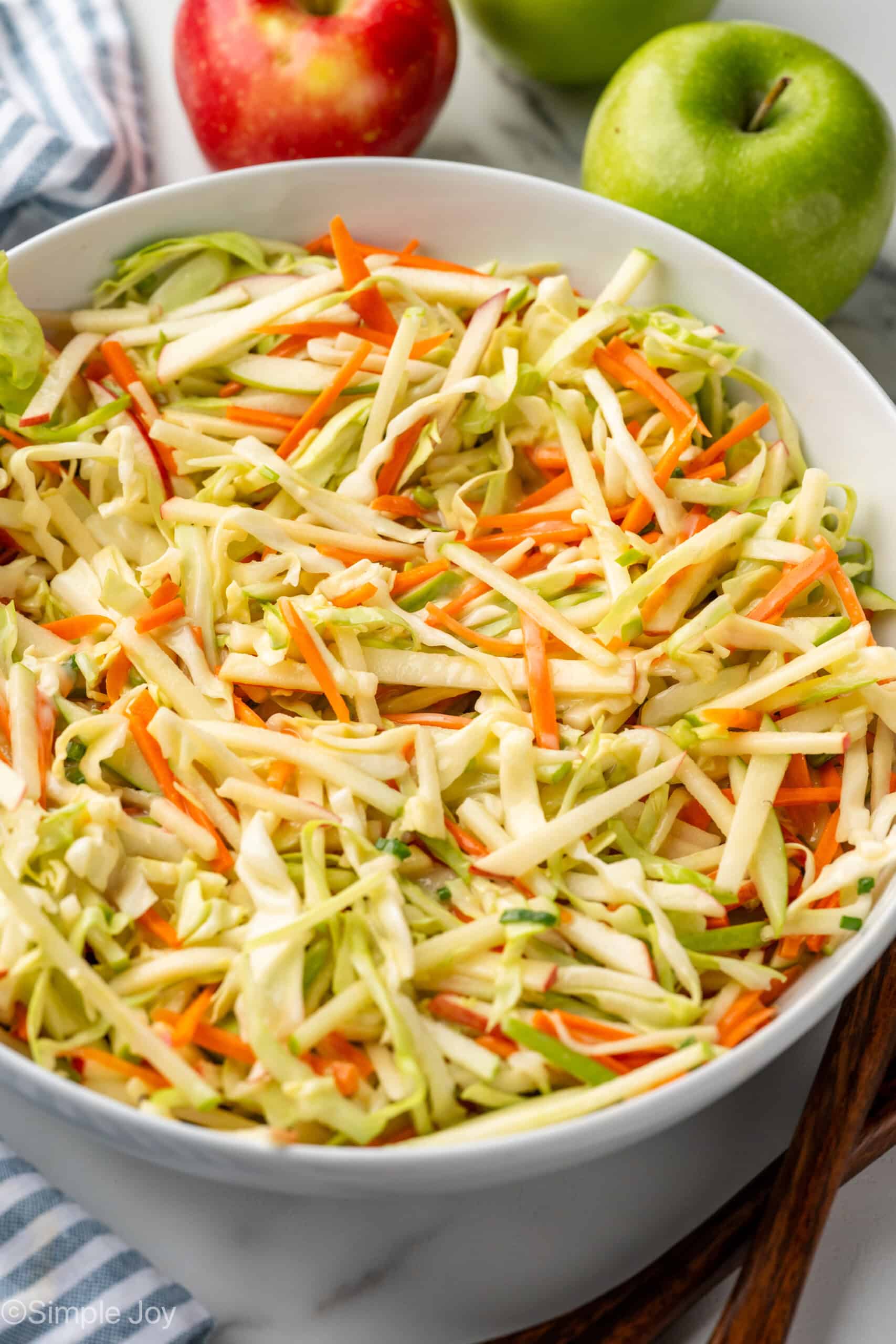 Bowl of apple slaw with red and green apples sitting in background