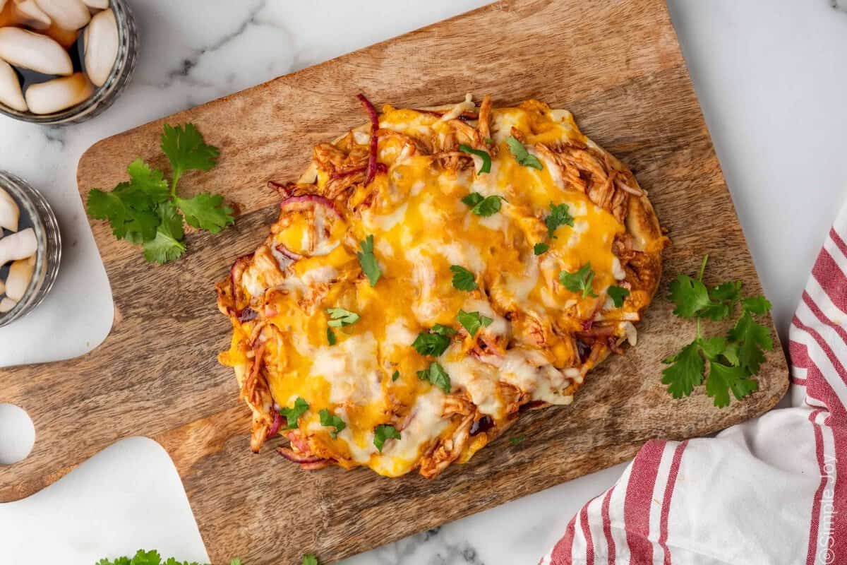 Overhead of BBQ Chicken Flatbread Pizza on a wooden cutting board garnished with fresh cilantro