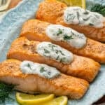 Platter of Broiled Salmon topped with Lemon Dill Sauce, fresh lemon slices and fresh dill sitting beside