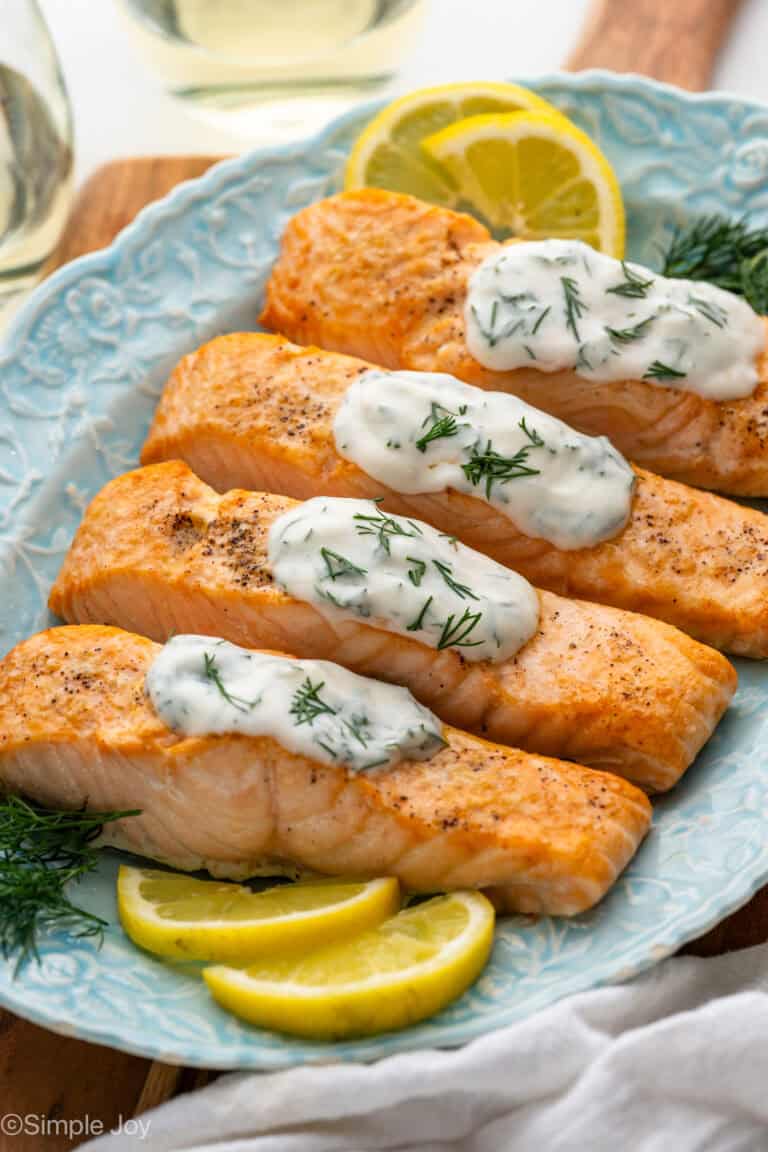 Platter of Broiled Salmon topped with Lemon Dill Sauce, fresh lemon slices and fresh dill sitting beside
