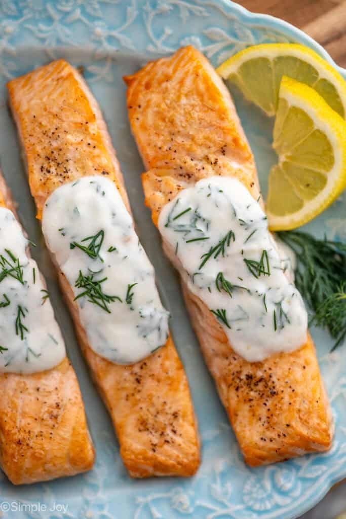Overhead of plate of Broiled Salmon with Lemon Dill Sauce, lemon slices and fresh dill sitting beside