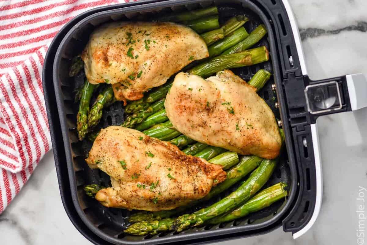 Overhead photo of air fryer chicken breasts in air fryer basket on top of asparagus