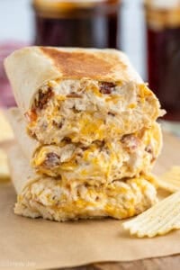 three crack chicken wraps stacked on top of each other with potato chips sitting beside
