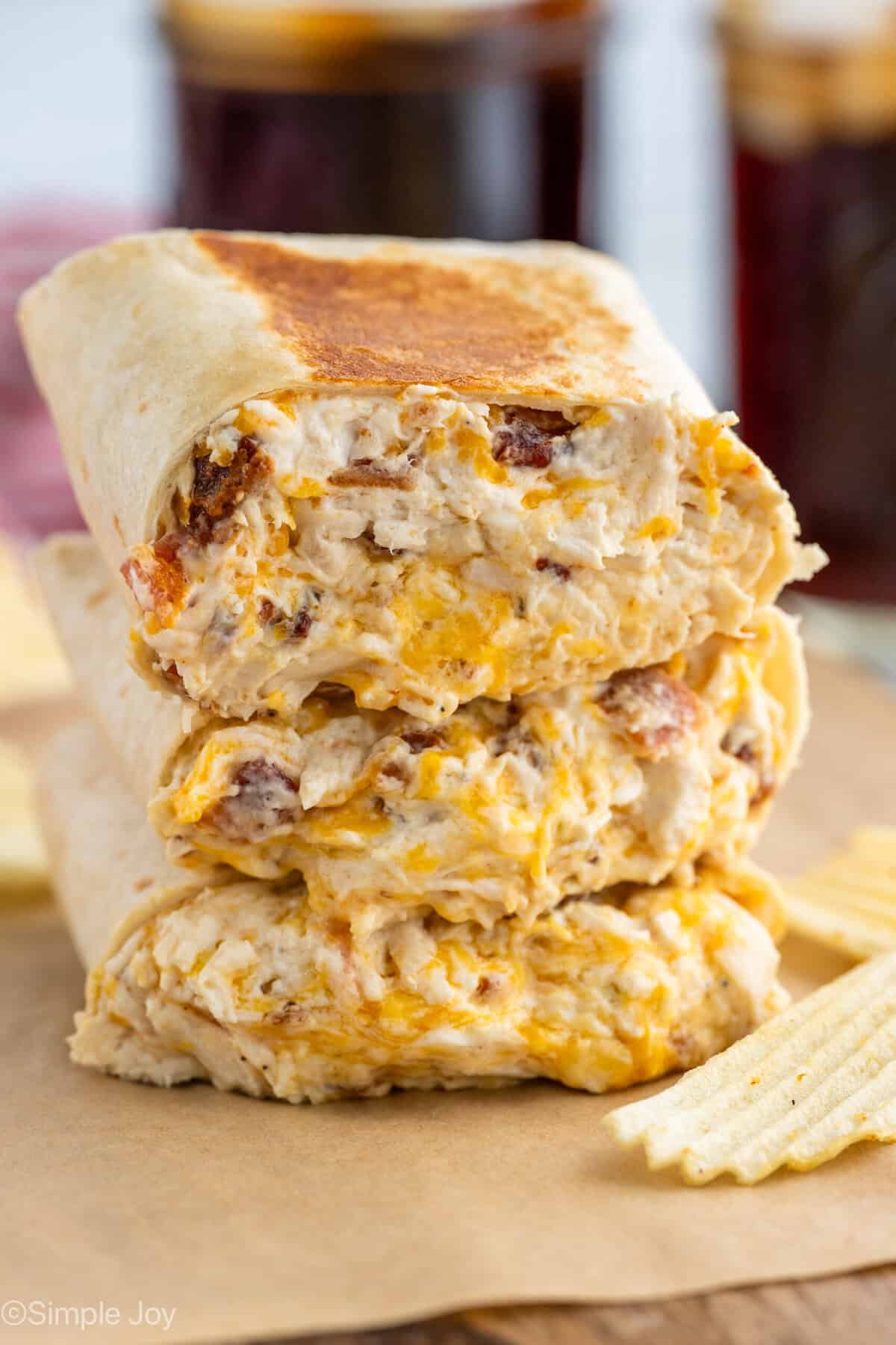 three crack chicken wraps stacked on top of each other with potato chips sitting beside