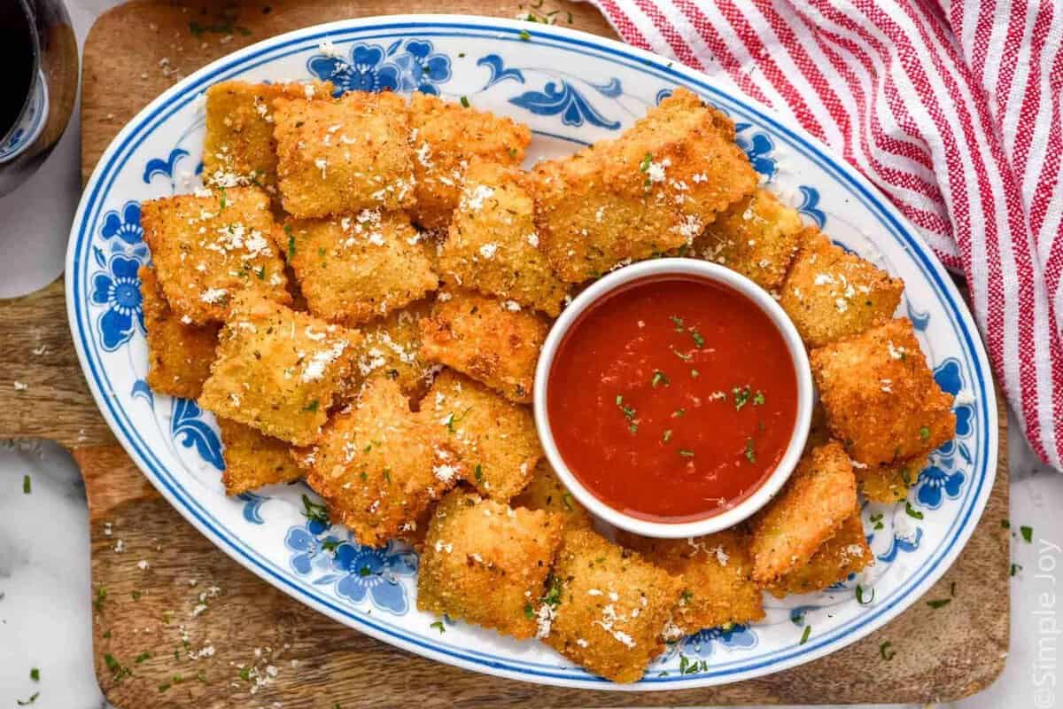 overhead of platter of Fried Ravioli topped with grated parmesan cheese, bowl of marinara sauce sitting in middle.