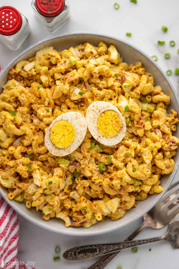 Overhead of bowl of Deviled Egg Pasta Salad garnished with two hard boiled egg halves and paprika, salt and pepper shakers and two forks sitting beside.