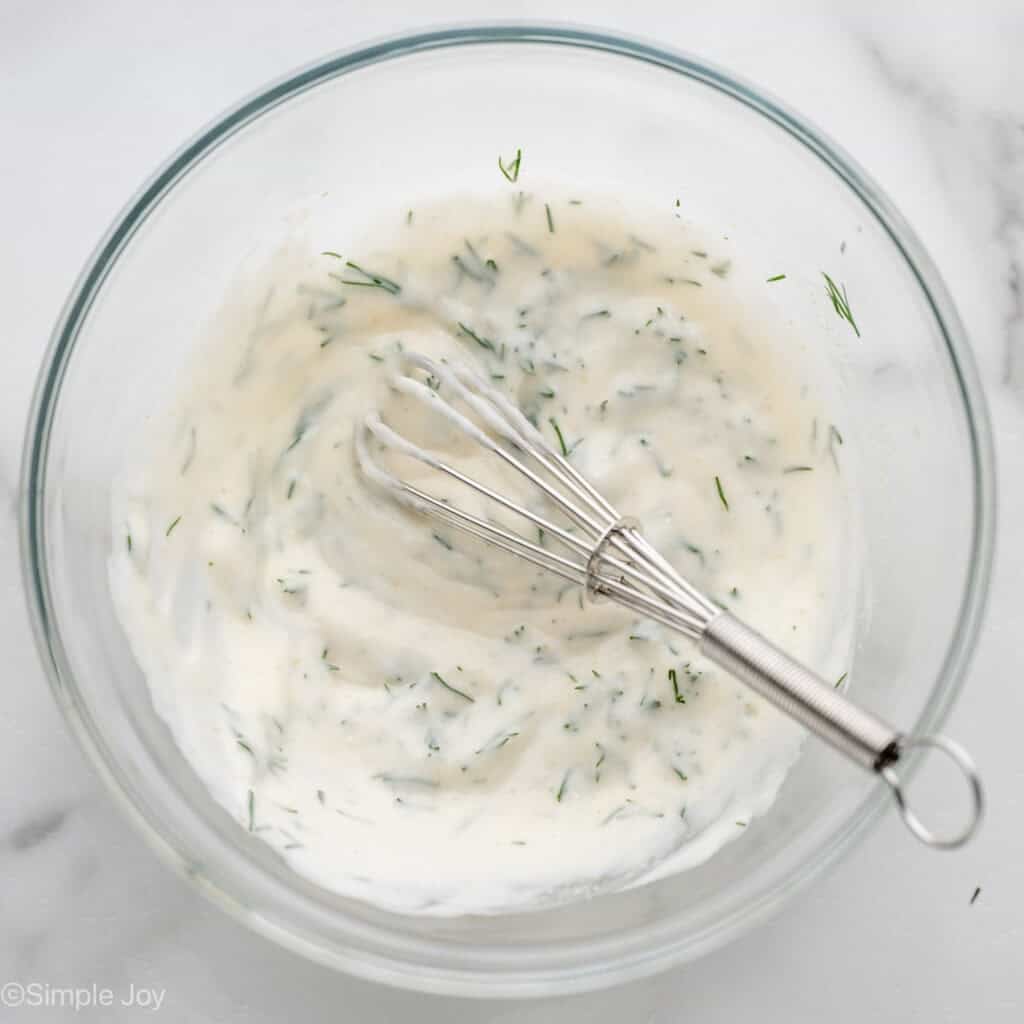 Overhead of bowl of lemon dill sauce ingredients and wire whisk to make broiled salmon