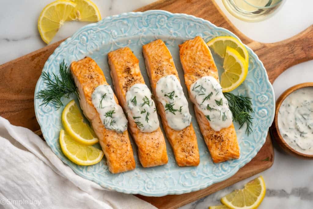 Overhead of platter of Broiled Salmon topped with Lemon Dill Sauce, garnished with lemon slices and fresh dill