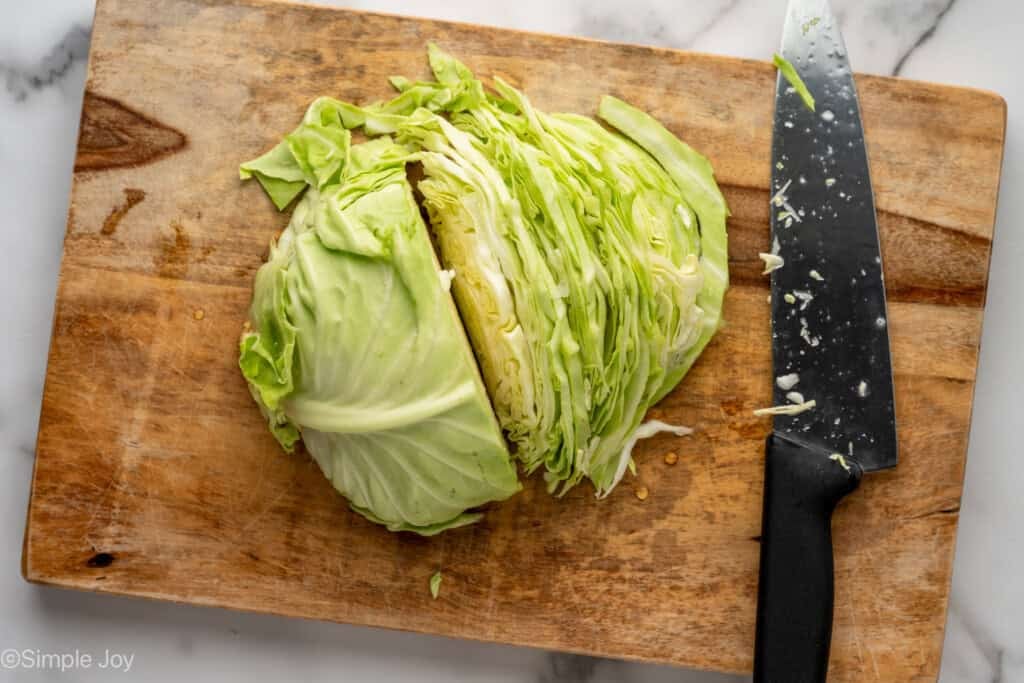 Overhead of head of lettuce with knife on wooden cutting board to make apple slaw