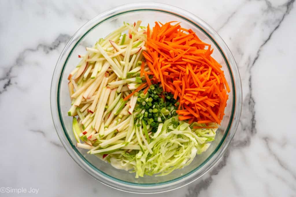Overhead of large glass bowl of apple slaw ingredients