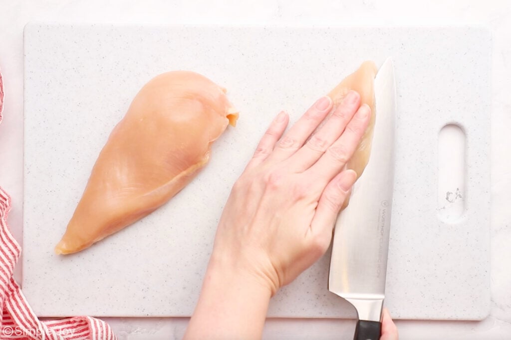 Person holding chicken breast and cutting into it with a large knife to make chicken cordon bleu