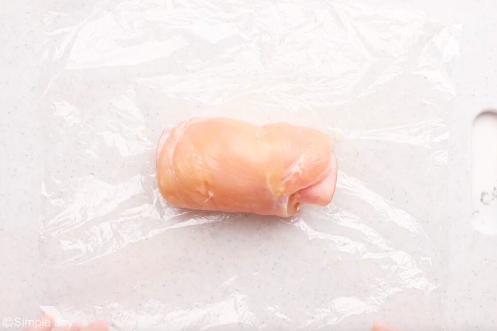 Overhead of chicken cordon bleu ingredients rolled up on a piece of plastic wrap