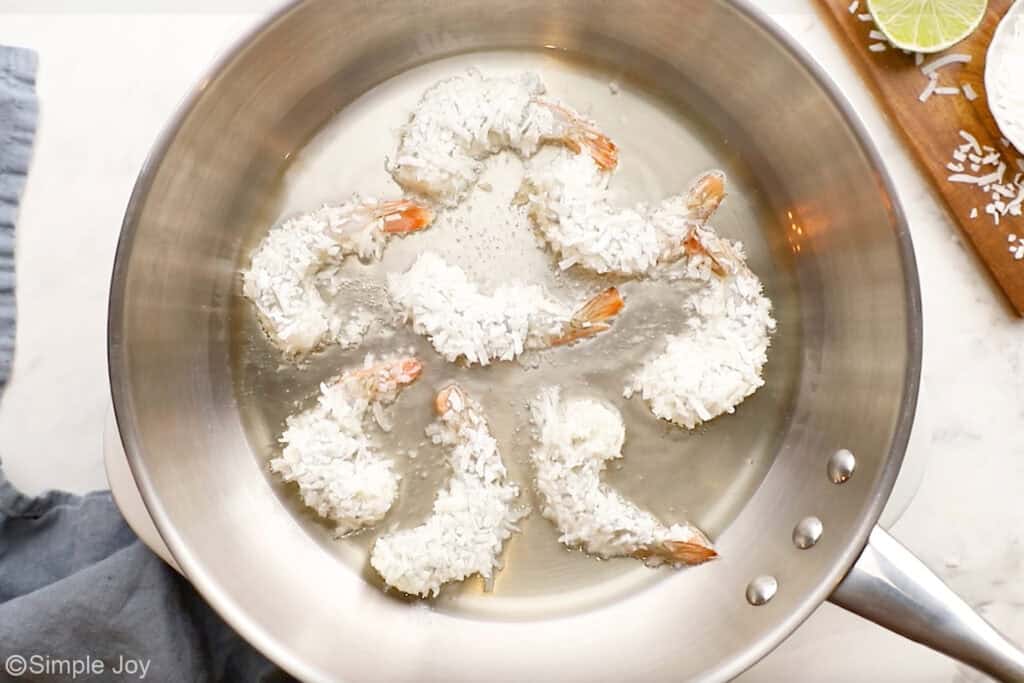 Overhead of coconut shrimp cooking in oil in skillet