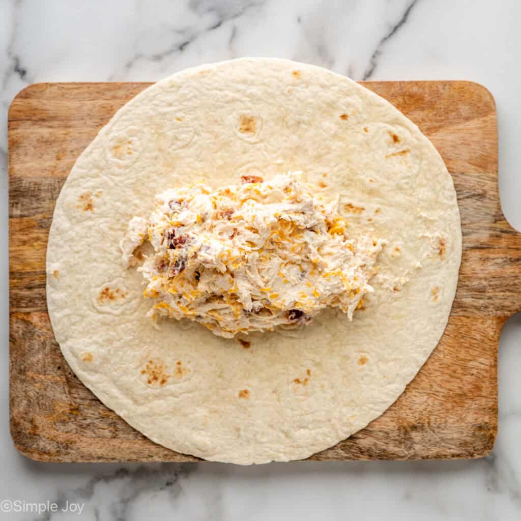 Overhead of tortilla on a wooden cutting board with crack chicken wrap ingredients