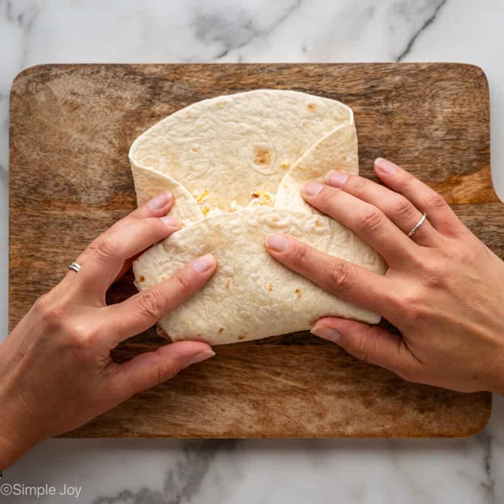 Overhead of person's hands folding tortilla to make crack chicken wrap