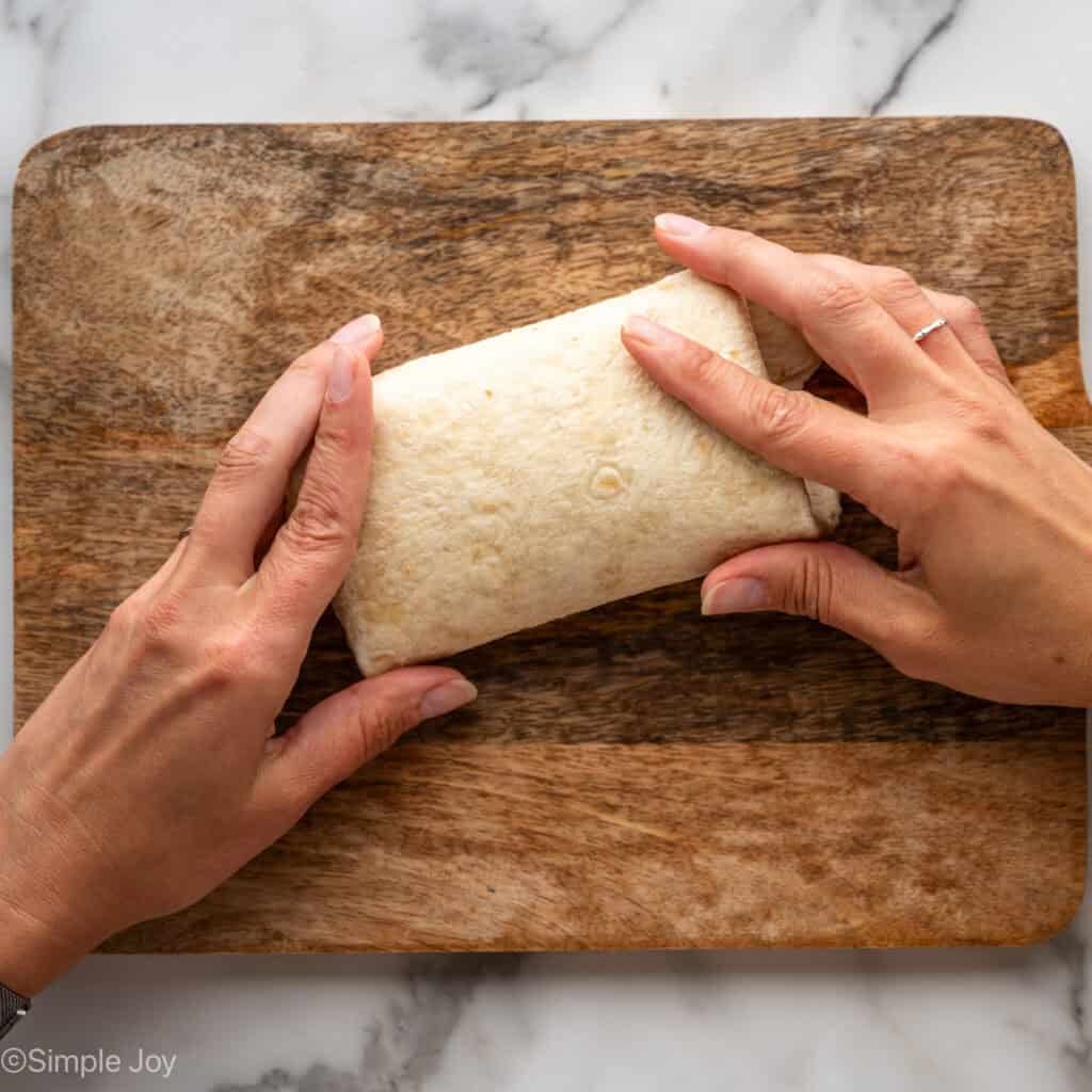 Overhead of hands folding tortilla to make crack chicken wrap