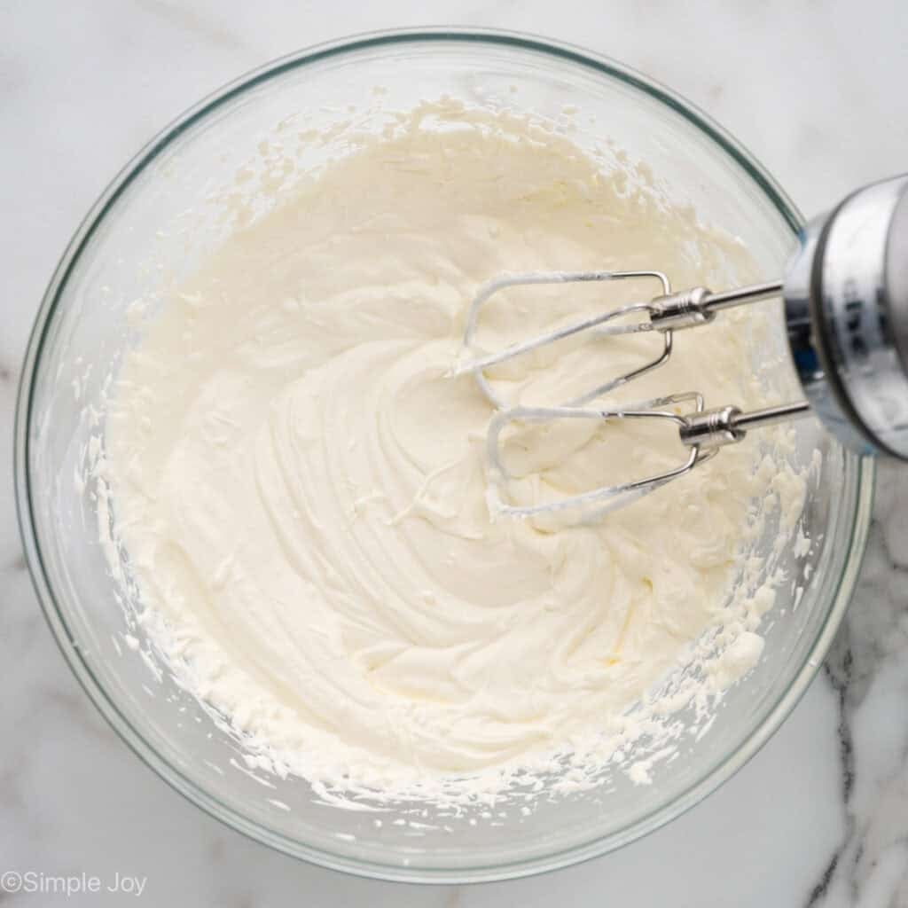 Overhead of glass bowl of crack dip ingredients with hand mixer